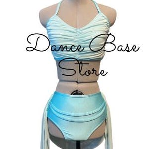 May include: A light blue two-piece dance outfit on a mannequin, featuring a ruched halter top and high-waisted bottoms with attached side panels. The text "Dance Base Store" is overlaid in black script across the center of the garment.