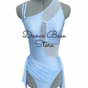 May include: A light blue leotard featuring a one-shoulder design with double straps, sheer mesh paneling, and a cutout at the midsection. The garment includes a gathered, draped fabric detail at the hip and displays the text Dance Base Store.