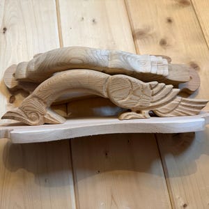 May include: Two light-colored wooden handles carved into the shape of birds with wings tucked against their bodies. Each handle features a curved neck and head at one end and a fanned tail at the other, mounted on a flat, rectangular wooden base.