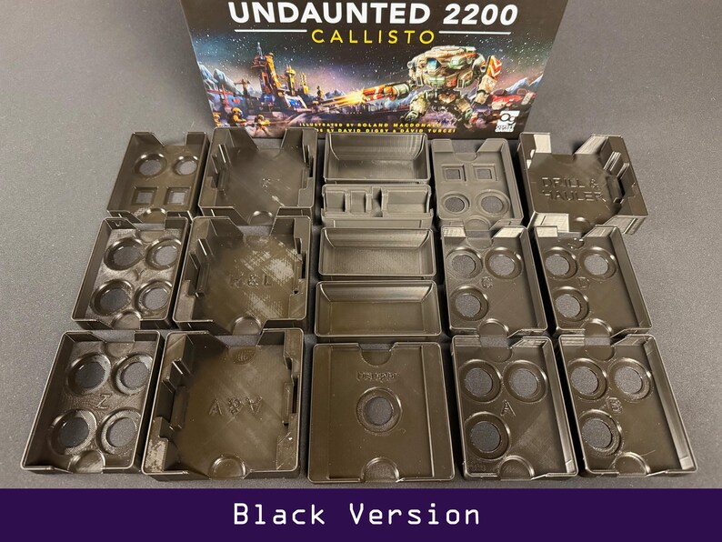 Peut inclure: Ensemble d'organisateurs de composants de jeu noirs, de formes et tailles vari&eacute;es, dispos&eacute;s en rang&eacute;es. La bo&icirc;te de jeu "Undaunted 2200 Callisto" est visible en arri&egrave;re-plan. Le texte "Black Version" est en bas.