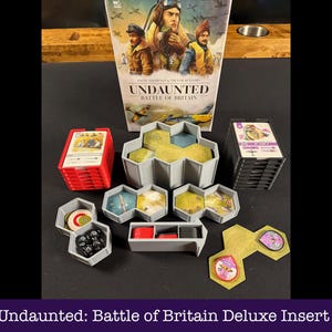 May include: A board game insert for "Undaunted: Battle of Britain". The image displays the game box, stacks of cards, hexagonal game tiles, and other components in red, grey, and yellow. The box art features illustrations of pilots and aircraft.