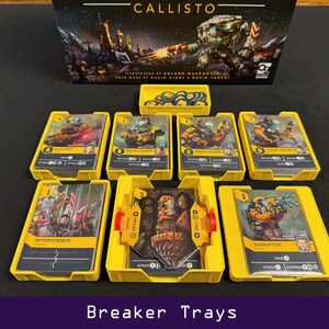 Peut inclure: Jeu de soci&eacute;t&eacute; "Callisto" avec des plateaux jaunes contenant des cartes de jeu. Les cartes pr&eacute;sentent des illustrations de personnages et des informations de jeu. L'illustration de la bo&icirc;te montre une ville futuriste et un grand robot.