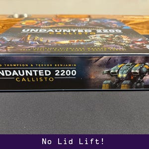 Peut inclure: Bo&icirc;te de jeu de soci&eacute;t&eacute; intitul&eacute;e "Undaunted 2200 Callisto" avec une illustration futuriste. La bo&icirc;te pr&eacute;sente les noms de David Thompson et Trevor Benjamin. L'illustration de la bo&icirc;te repr&eacute;sente un v&eacute;hicule futuriste et une sc&egrave;ne de bataille spatiale.