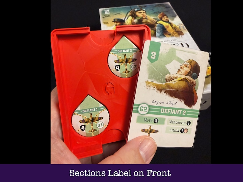 May include: A red plastic game component holder with two circular cutouts, each containing a game piece with a plane graphic. A game card with a pilot illustration and the text "DEFIANT 2" is held next to the holder. The text "Sections Label on Front" is at the bottom.