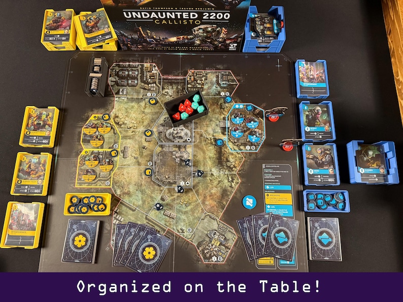Peut inclure: Mise en place d'un jeu de soci&eacute;t&eacute; avec un plateau de jeu d&eacute;taill&eacute;, des cartes et divers &eacute;l&eacute;ments de jeu. Le jeu comprend des porte-cartes jaunes et bleus, des d&eacute;s et une bo&icirc;te avec le titre du jeu "Undaunted 2200 Callisto". Le texte "Organized on the Table!" est en bas.