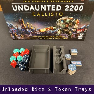 Peut inclure: Une bo&icirc;te de jeu de soci&eacute;t&eacute; intitul&eacute;e "Undaunted 2200 Callisto" avec une sc&egrave;ne de bataille spatiale. En dessous, des plateaux gris, des d&eacute;s rouges, turquoise et bleus, et des piles de jetons de jeu. Le texte "Unloaded Dice & Token Trays" est en bas.