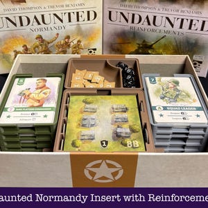 以下が含まれることがあります： Undaunted NormandyおよびReinforcementsボードゲーム用のボックスインサート。緑と灰色のトレイに入った2つのカードスタック、建物のイラストが描かれた中央のタイル、ベージュの丸いトークンが入ったコンパートメント、黒いサイコロが収められています。