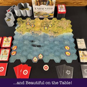 May include: A board game set up on a table, featuring a hexagonal game board with a coastal map. The game includes cards, dice, and tokens. The box reads "Undaunted: Battle of Britain". The text at the bottom reads "...and Beautiful on the Table!"