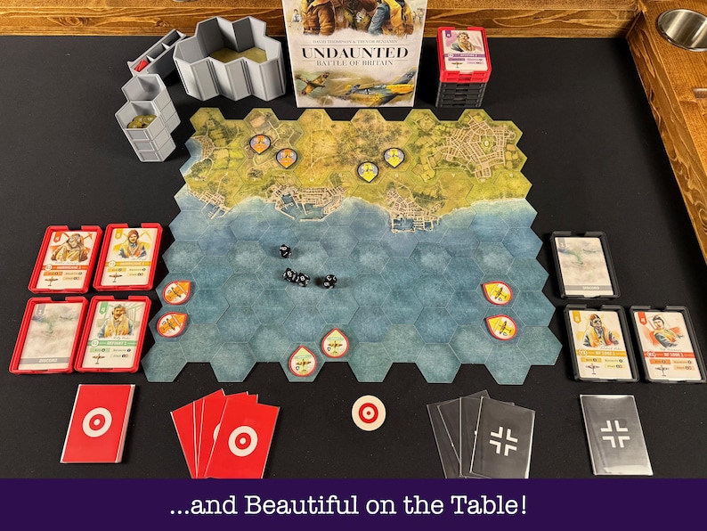 May include: A board game set up on a table, featuring a hexagonal game board with a coastal map. The game includes cards, dice, and tokens. The box reads "Undaunted: Battle of Britain". The text at the bottom reads "...and Beautiful on the Table!"