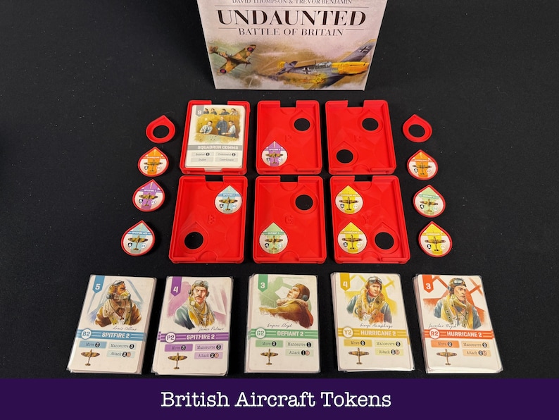 May include: A board game set, "Undaunted: Battle of Britain", featuring red game piece holders, cards, and tokens. The cards display pilot illustrations and aircraft. The game components are arranged on a black surface. The text "British Aircraft Tokens" is at the bottom.