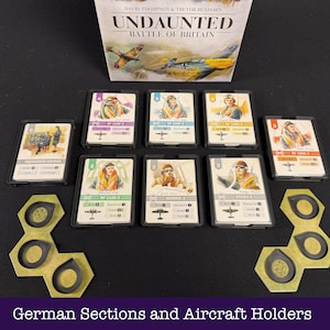 May include: The board game "Undaunted: Battle of Britain" is displayed with pilot cards and hexagonal aircraft holders. The game's box is visible, and the scene is set on a black surface.
