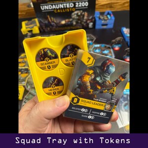 Peut inclure: Un plateau de jeu jaune avec des jetons et des cartes du jeu de soci&eacute;t&eacute; Undaunted 2200 Callisto. Le plateau contient des jetons "Scanner", "Blaster" et "Hewer". Une carte montre un chef d'escouade avec des statistiques. Le texte "Squad Tray with Tokens" est en bas.