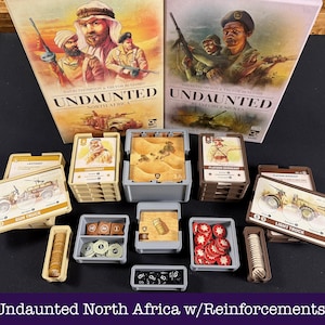 Può includere: Due scatole di giochi da tavolo intitolate Undaunted North Africa e Undaunted Reinforcements, accompagnate da vari portacarte in plastica, vassoi per gettoni e pile di carte da gioco con illustrazioni militari e testo come Gun Truck.