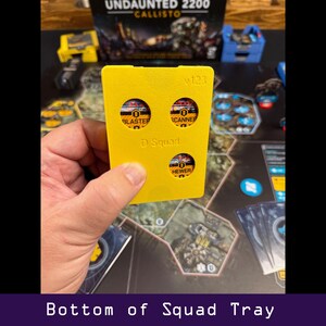 Peut inclure: Un plateau de jeu jaune pour le jeu de soci&eacute;t&eacute; Undaunted 2200: Callisto, avec trois d&eacute;coupes circulaires &eacute;tiquet&eacute;es "Blaster", "Scanner" et "Hewer". Le plateau est &eacute;tiquet&eacute; "D Squad" et "v123". Le texte "Bottom of Squad Tray" est en bas.