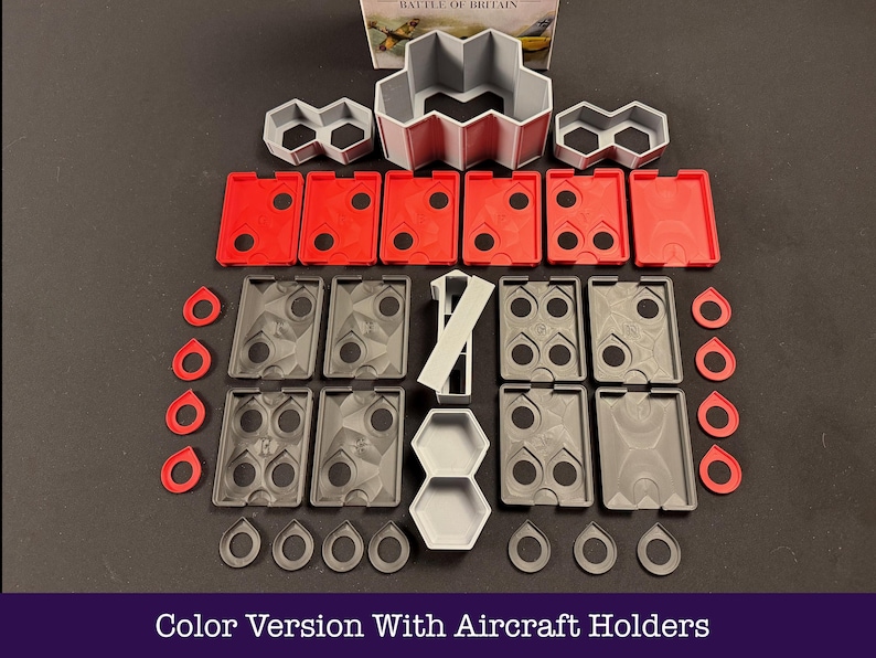 May include: A selection of grey, red, and white game components, including aircraft holders, displayed on a dark surface. The set features diverse shapes and sizes, such as rectangular, hexagonal, and circular pieces. The text "Color Version With Aircraft Holders" is at the bottom.