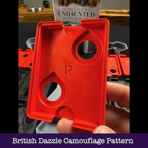 May include: A vibrant red plastic game piece featuring two circular openings and a "P" logo. The rectangular component has a textured surface. The text "British Dazzle Camouflage Pattern" is displayed at the bottom of the image.
