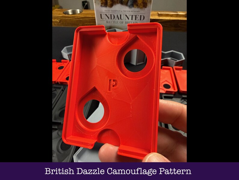 May include: A vibrant red plastic game piece featuring two circular openings and a "P" logo. The rectangular component has a textured surface. The text "British Dazzle Camouflage Pattern" is displayed at the bottom of the image.