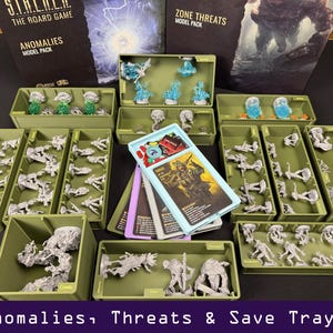 May include: A collection of board game components, including miniature figures, cards, and model packs. The figures are in various poses and colors, stored in green trays. The text "Anomalies, Threats & Save Trays!" is at the bottom.