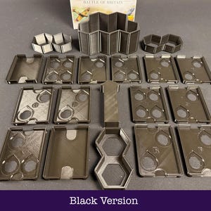 May include: An assortment of black game components, featuring rectangular trays with circular apertures, hexagonal forms, and a concertina-style structure. The text "Black Version" is at the base of the image. The pieces are displayed on a dark surface.