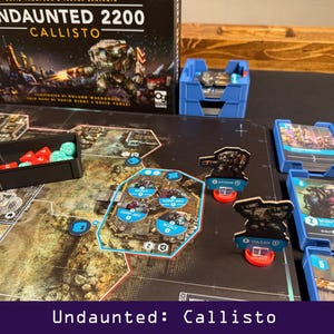 Peut inclure: Mise en place du jeu de soci&eacute;t&eacute; "Undaunted: Callisto". Le plateau de jeu pr&eacute;sente une carte d&eacute;taill&eacute;e avec des pi&egrave;ces, notamment des cartes, des d&eacute;s et des figurines miniatures. La bo&icirc;te de jeu et les conteneurs de rangement bleus sont &eacute;galement visibles.