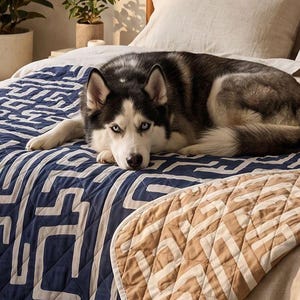 May include: A reversible quilted throw blanket featuring a dark navy blue side with a white geometric maze pattern and a tan side with a white geometric maze pattern, draped over a bed with a black and white husky dog resting on top of it.