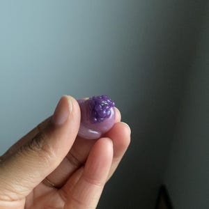 May include: A small, round, purple jelly candy with a cluster of smaller purple jelly candies on top.
