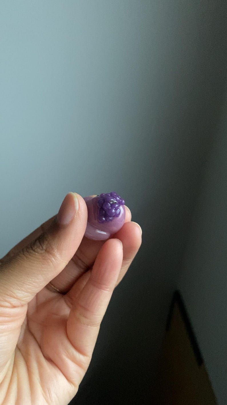 May include: A small, round, purple jelly candy with a cluster of smaller purple jelly candies on top.