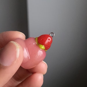May include: A pink and red glass charm shaped like a strawberry with a silver loop for hanging.