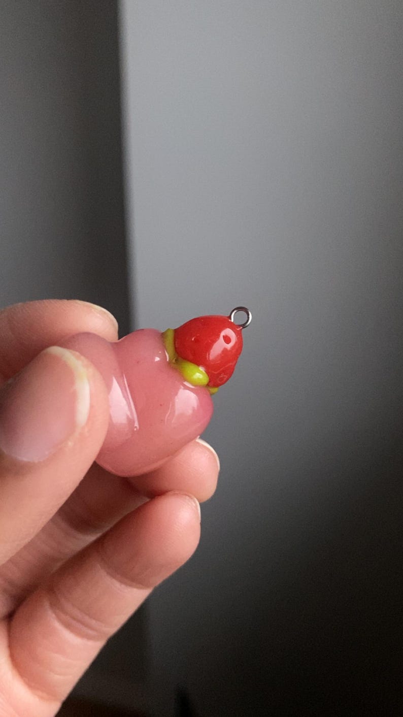 May include: A pink and red glass charm shaped like a strawberry with a silver loop for hanging.