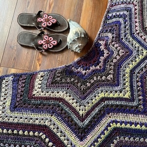 May include: A crocheted shawl with a starburst pattern in shades of purple, brown, and yellow. The shawl is made with a variety of stitches and textures, creating a unique and eye-catching design.
