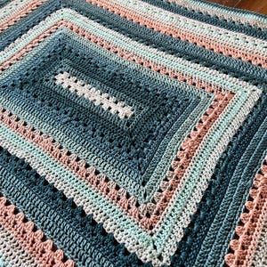 May include: A crocheted blanket with a square pattern in shades of teal, mint green, and peach.