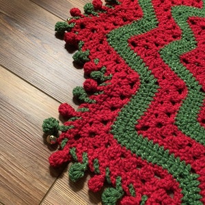 May include: A red and green crocheted Christmas tree skirt with a sparkly finish and a scalloped edge. The skirt has a fringe of green and red pom-poms.