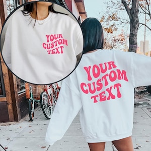 May include: White sweatshirt with pink text that says "YOUR CUSTOM TEXT" on the front and back.
