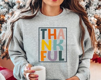 May include: A gray sweatshirt with the word "THANKFUL" printed in colorful block letters.