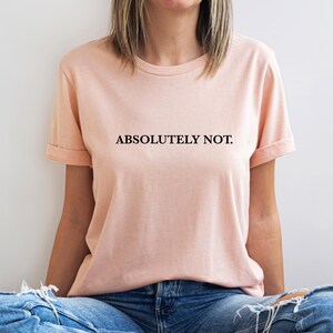 Puede incluir: Una camiseta de color melocot&oacute;n con el texto "ABSOLUTELY NOT." impreso en negro.