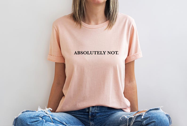 Puede incluir: Una camiseta de color melocot&oacute;n con el texto "ABSOLUTELY NOT." impreso en negro.