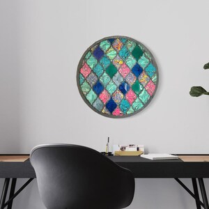 May include: A round wall decor with a mosaic design featuring a repeating pattern of teal, blue, pink, and green diamond shapes. The mosaic is set in a silver frame.