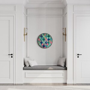 May include: A white hallway with two white doors and a white bench with gray cushions. A round wall art piece with a geometric pattern of blue, green, pink, and white squares is hanging on the wall.