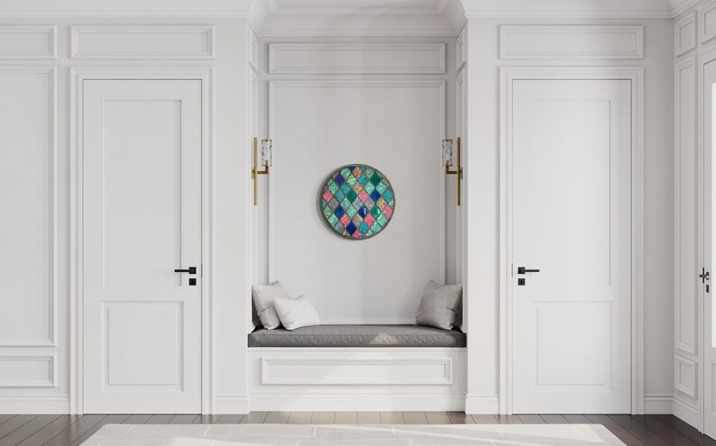 May include: A white hallway with two white doors and a white bench with gray cushions. A round wall art piece with a geometric pattern of blue, green, pink, and white squares is hanging on the wall.