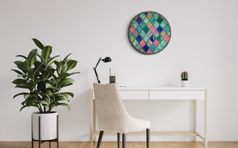 May include: A white desk with a beige chair and a round wall decor with a mosaic design in shades of blue, green, pink, and white. A potted plant and a small cactus are on the desk.