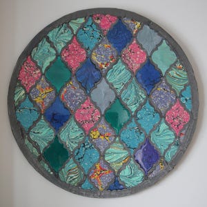 May include: A round, decorative wall hanging with a mosaic design. The mosaic is made of small, colorful tiles in shades of blue, green, pink, and purple. The tiles are arranged in a geometric pattern, creating a visually appealing and intricate design.