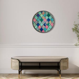 May include: A round wall art piece with a geometric pattern of teal, blue, pink, and white squares. The art is framed in a dark gray circle.