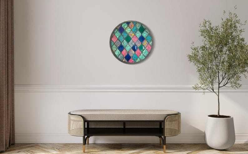May include: A round wall art piece with a geometric pattern of teal, blue, pink, and white squares. The art is framed in a dark gray circle.