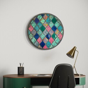 May include: A round wall art piece with a mosaic design. The mosaic is made up of small, colorful tiles in shades of blue, green, pink, and white. The tiles are arranged in a geometric pattern.