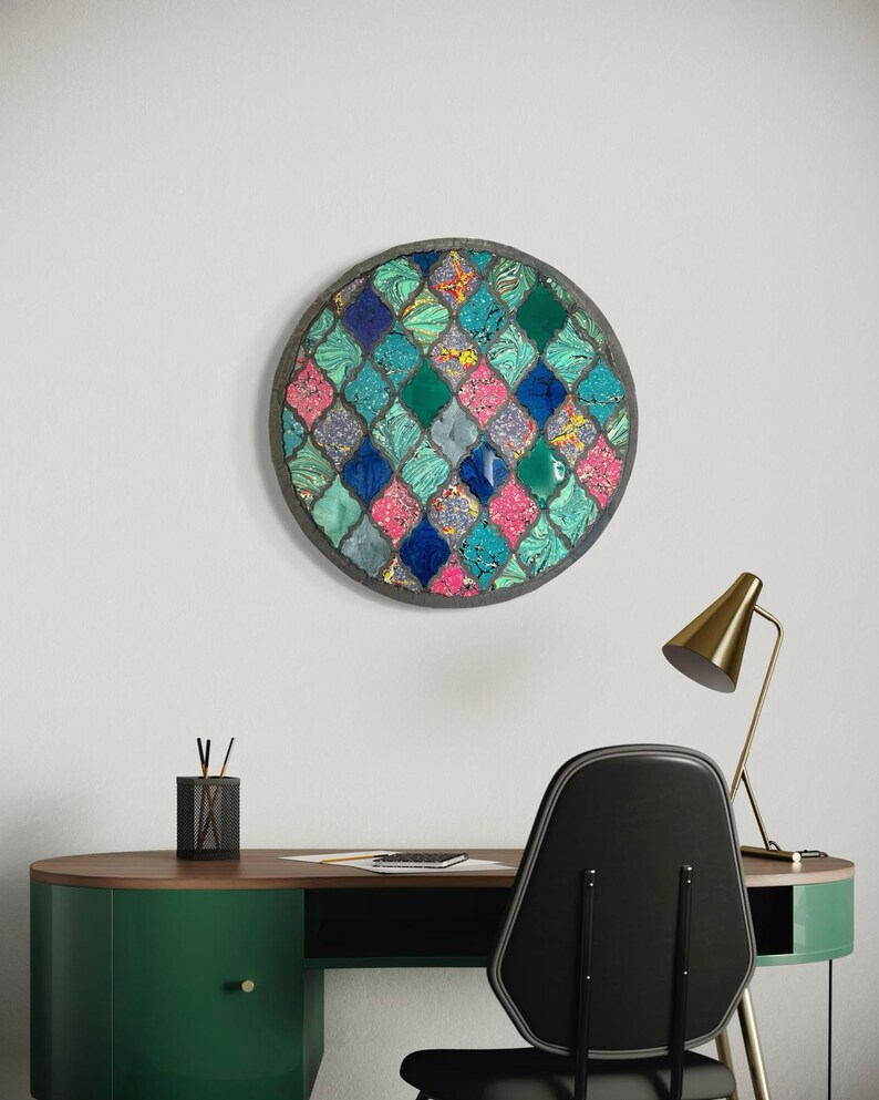 May include: A round wall art piece with a mosaic design. The mosaic is made up of small, colorful tiles in shades of blue, green, pink, and white. The tiles are arranged in a geometric pattern.