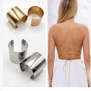 Op de afbeelding: Een set van twee goudkleurige metalen manchetten en twee zilverkleurige metalen manchetten, samen met een rugloze top met dunne goudkleurige veters die over de rug kruisen. De afbeelding bevat de tekst (Option 2) en Matching cuffs and laces on the back.