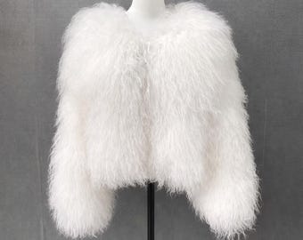 Könnte beinhalten: Eine weiße Kunstfelljacke mit rundem Ausschnitt und langen Ärmeln. Die Jacke wird auf einer Schaufensterpuppe vor grauem Hintergrund präsentiert. Das Fell ist voluminös und weich, was einen luxuriösen Look erzeugt.