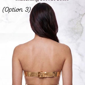 Op de afbeelding: Een metallic goudkleurig korset met twee horizontale riemsluitingen met bijpassende gouden gespen. De tekst "Belt Closure matching corset color (Option 3)" staat in het zwart boven het kledingstuk gedrukt. Het ontwerp bestaat uit twee banden.