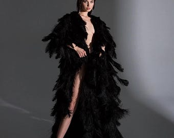 Könnte beinhalten: Eine Frau trägt ein langes schwarzes Federkleid mit einem Schlitz an der Seite. Das Kleid besteht aus vielen Schichten Federn und hat eine fließende Silhouette.