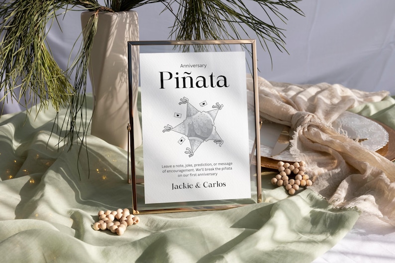 May include: A framed sign with the text "Anniversary Pi&ntilde;ata" and instructions to leave a note, joke, prediction, or message of encouragement. The sign also includes the names "Jackie & Carlos".